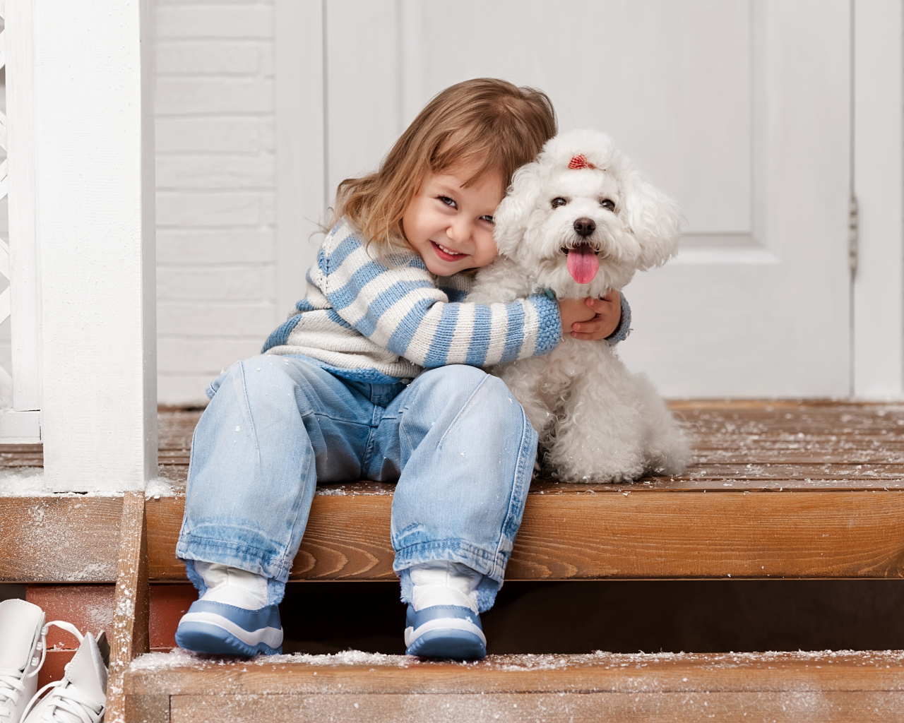 Маленькая улыбающаяся девочка сидит с белым пуделем на ступеньках