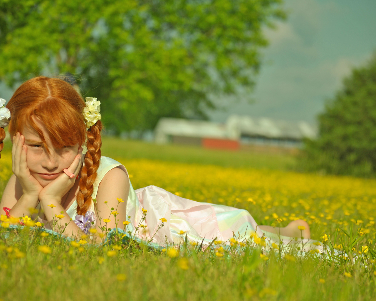 Рыжеволосая девочка с косичками лежит на зеленой траве