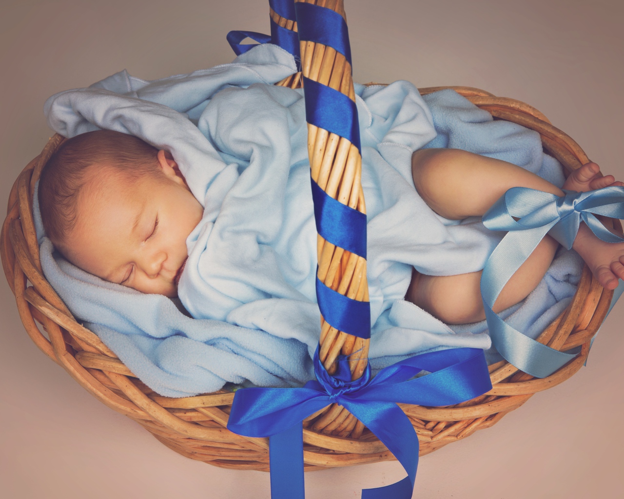 Спящий грудной ребенок в корзине с синими лентами