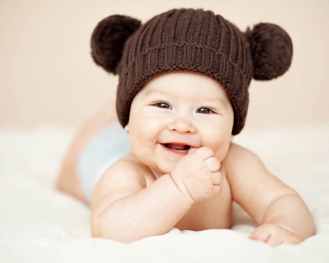 Улыбающийся грудной ребенок в коричневой вязаной шапке