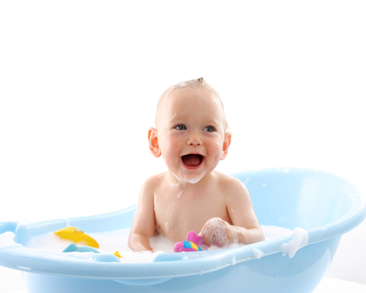 Улыбающийся грудной ребенок сидит в синей ванночке на белом фоне