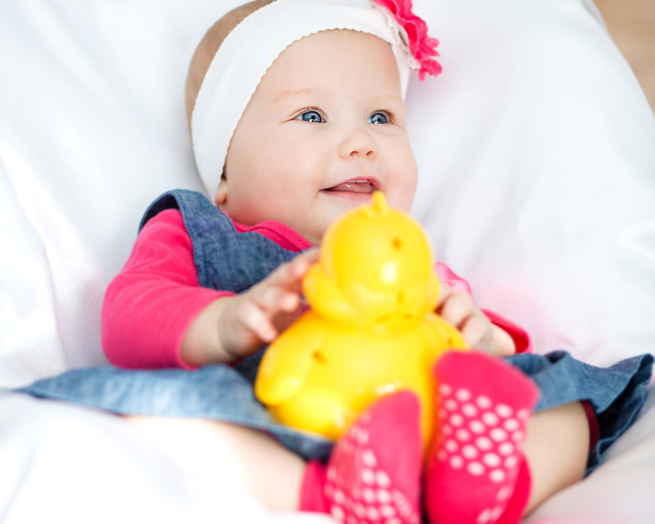 Улыбающаяся голубоглазая девочка младенец с игрушкой в руках