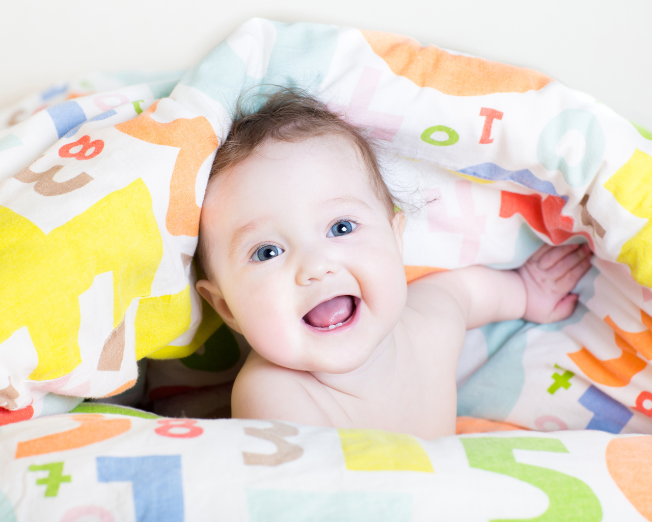 Улыбающийся голубоглазый ребенок под разноцветным покрывалом