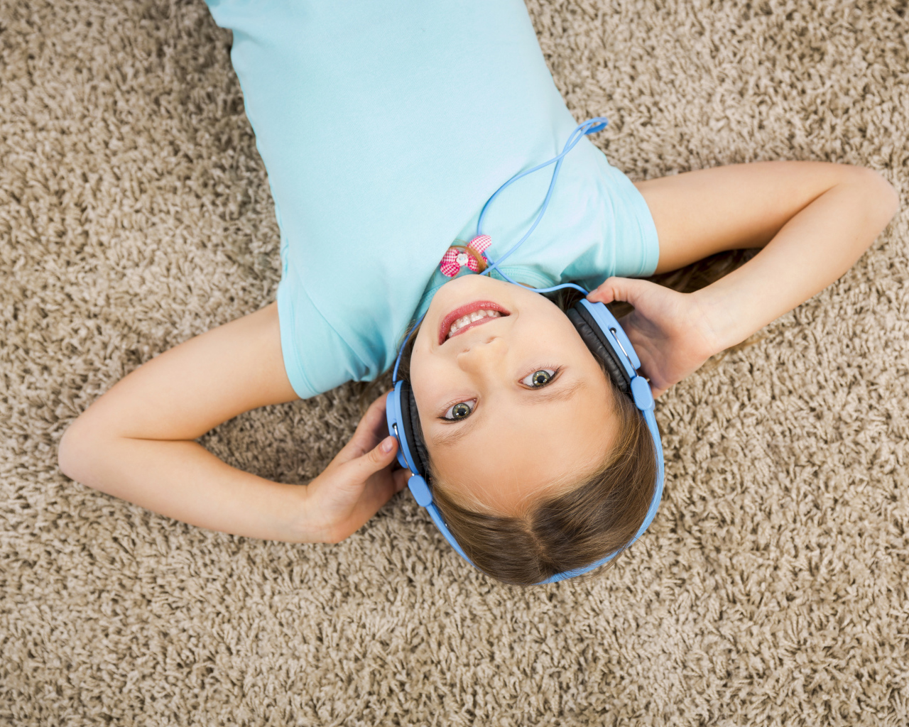 Улыбающаяся девочка в больших голубых наушниках