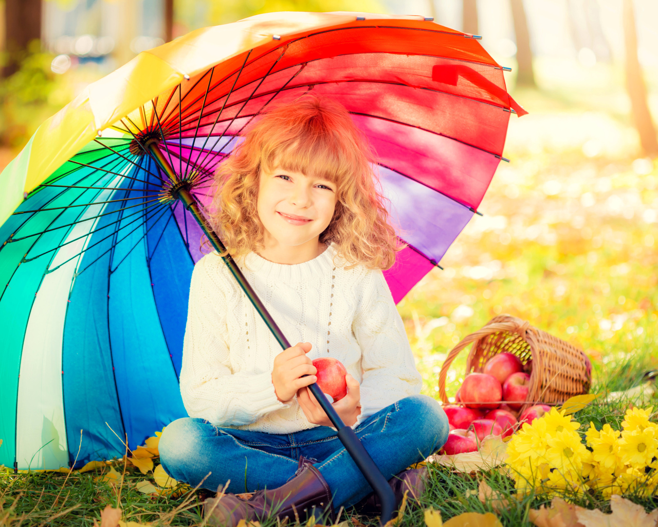 Улыбающаяся девочка под сидит под разноцветным зонтом