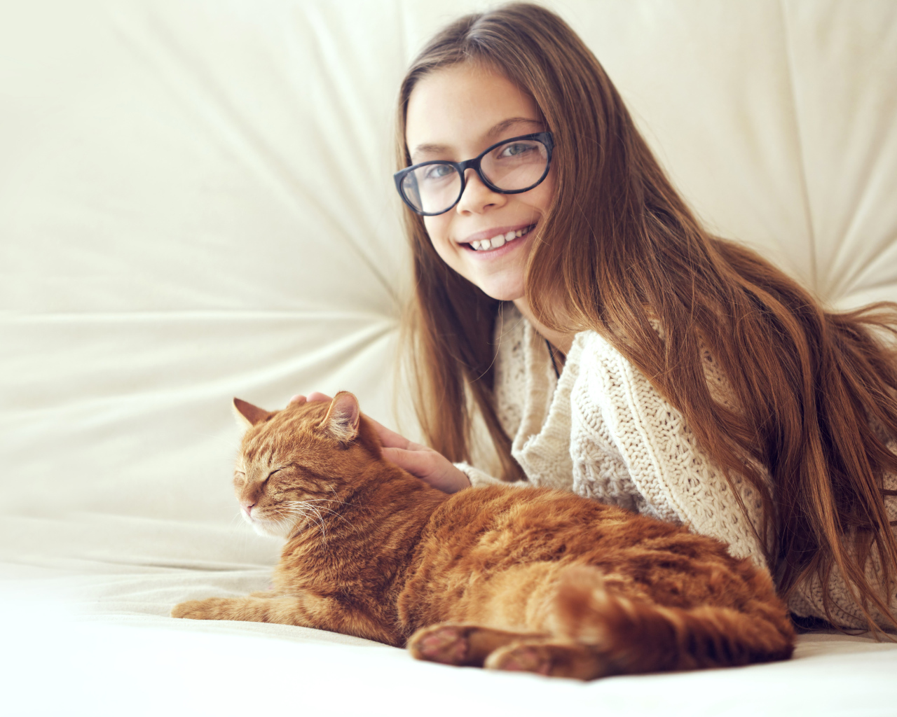 Улыбающаяся девочка шатенка в очках гладит рыжего кота