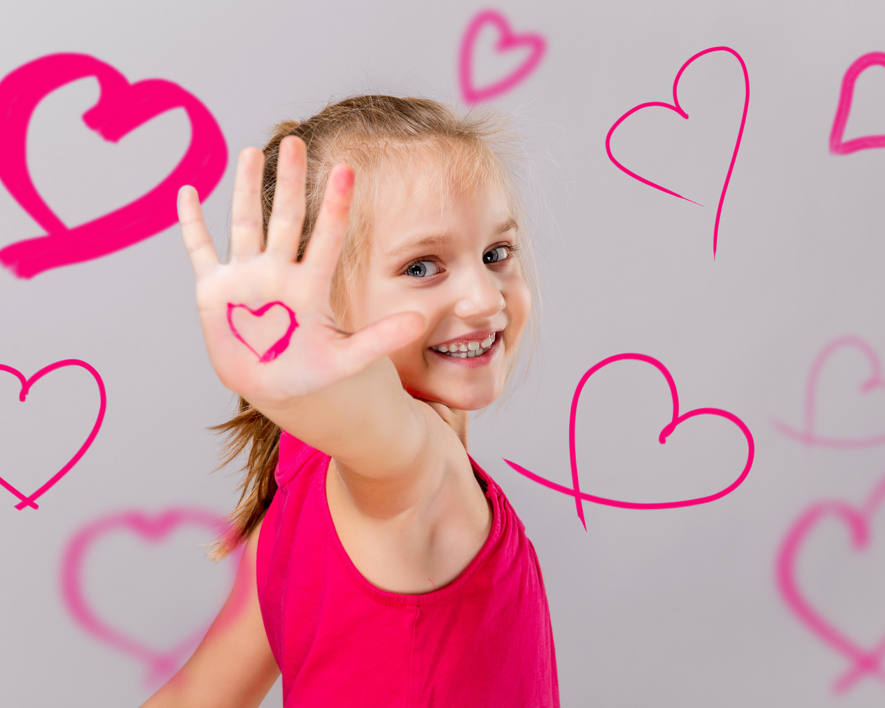 Улыбающаяся девочка с нарисованными сердечками на сером фоне