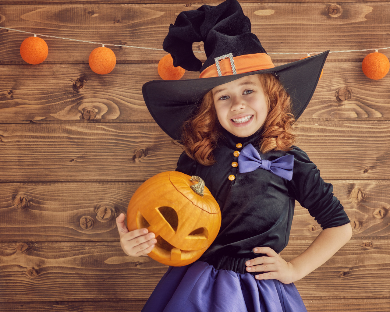 Улыбающаяся маленькая девочка в костюме ведьмы с тыквой на Хэллоуин