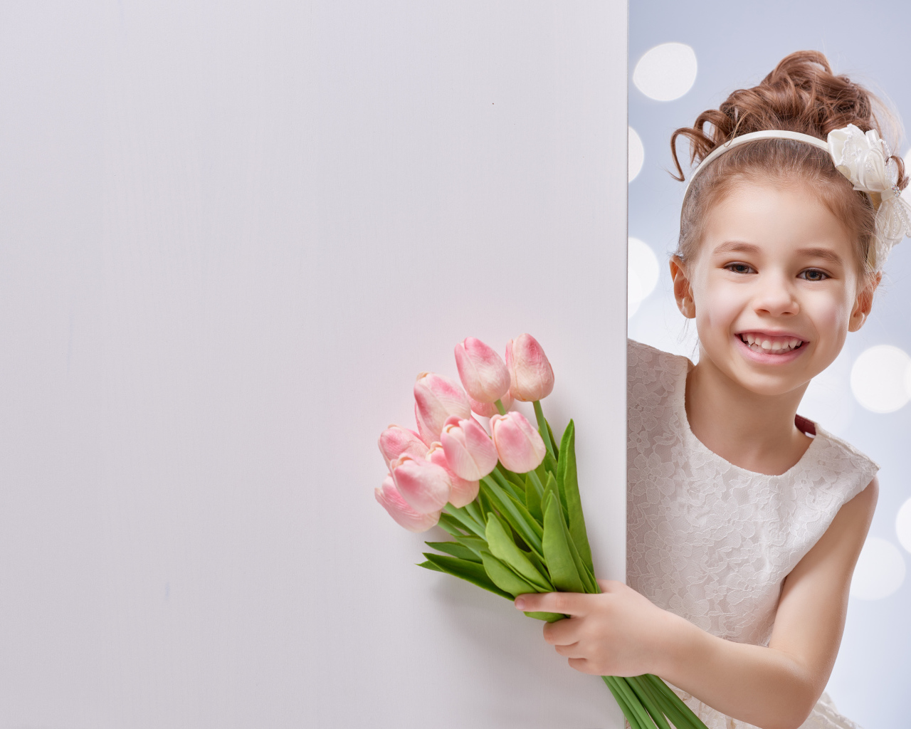 Улыбающаяся маленькая девочка с букетом розовых тюльпанов