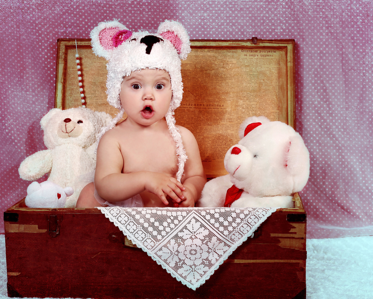 Удивленный малыш сидит в сундуке с мягкими игрушками