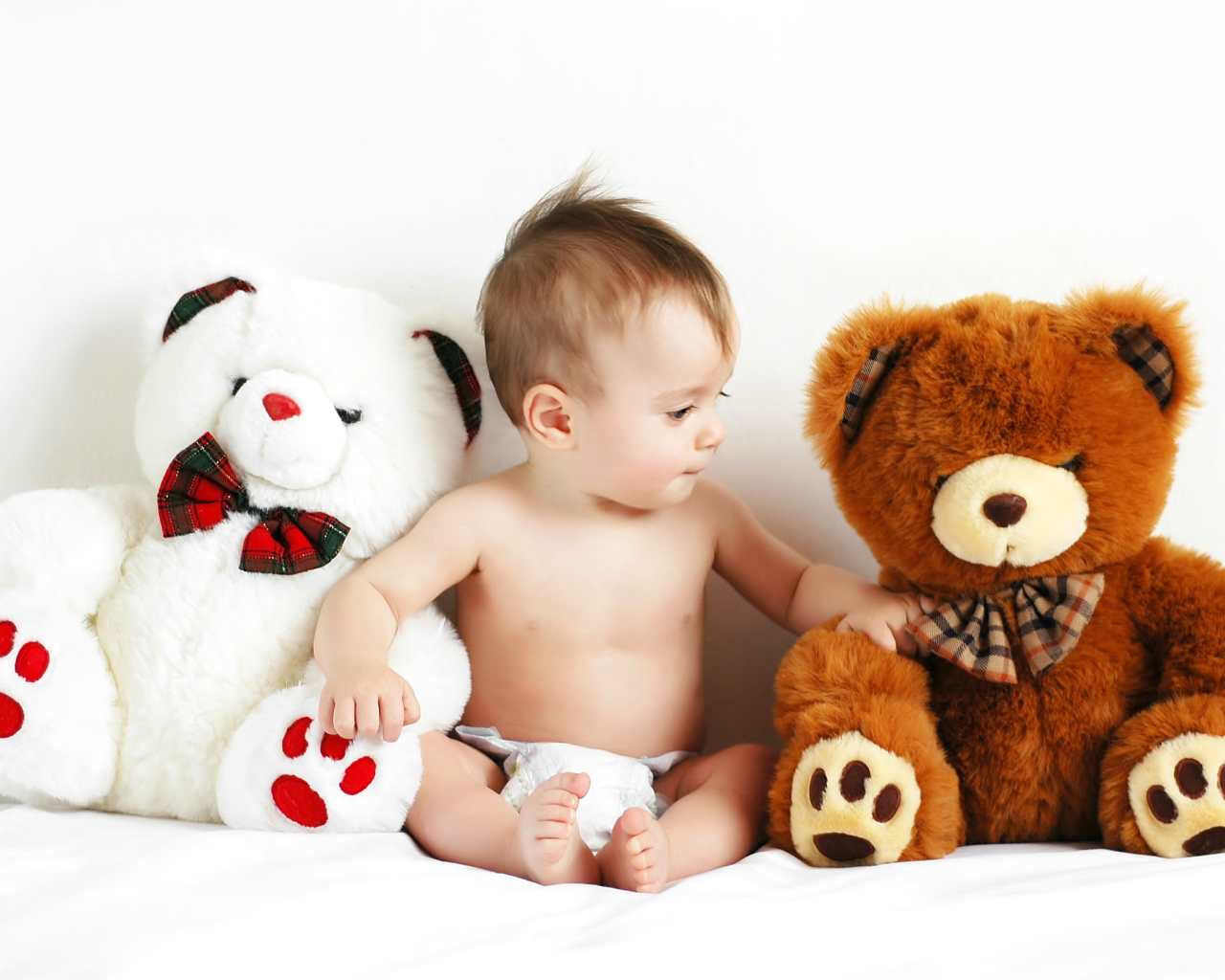 Младенец сидит с двумя большими плюшевыми медведями