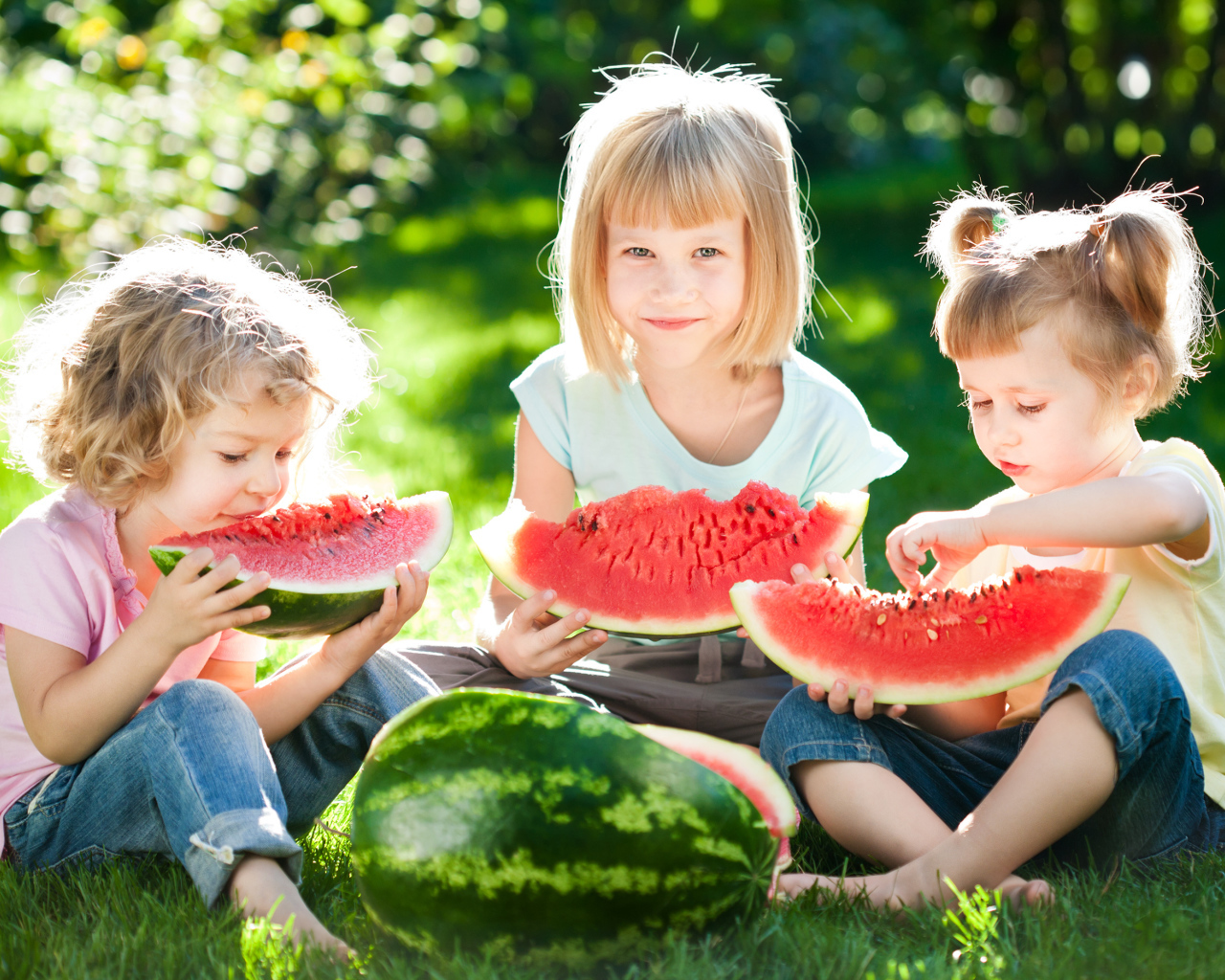 Три маленькие девочки едят арбуз на зеленой траве летом