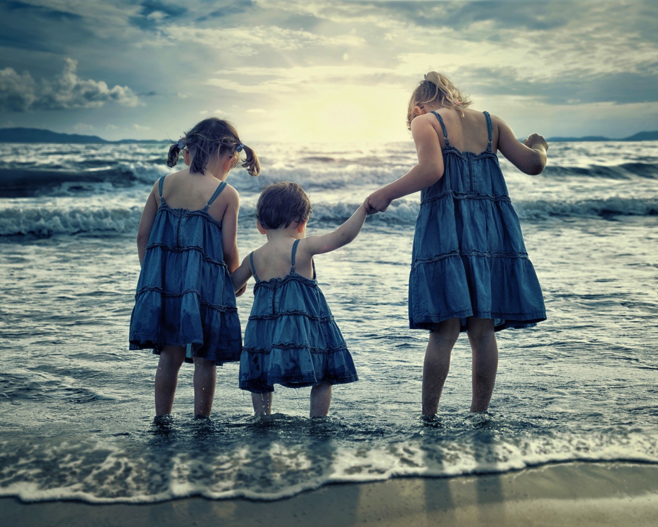 Три маленькие девочки стоят в воде на берегу моря