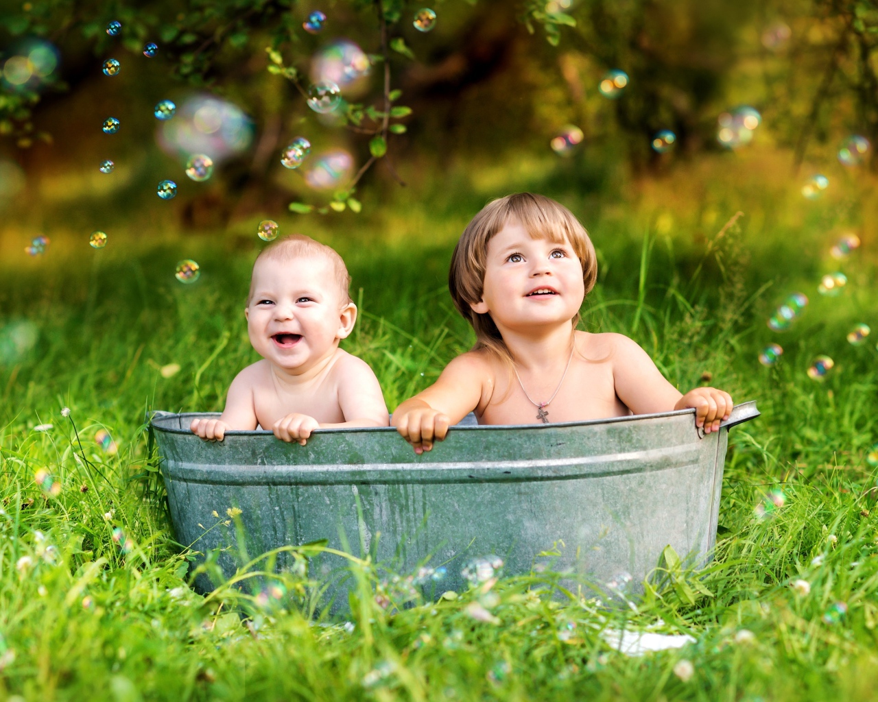 Два маленьких ребенка сидят в железном корыте на зеленой траве