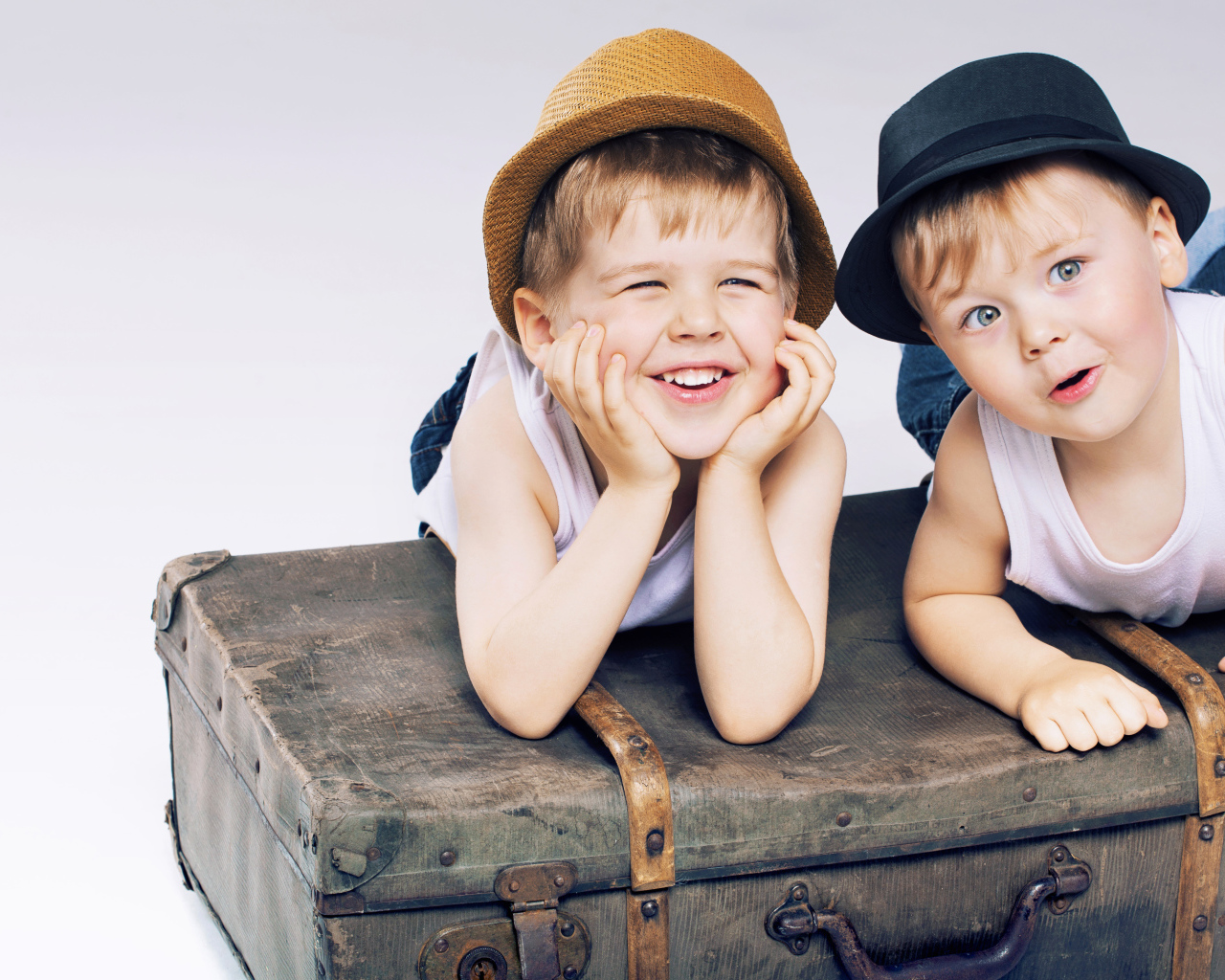 Два маленьких улыбающихся мальчика лежат на старом чемодане