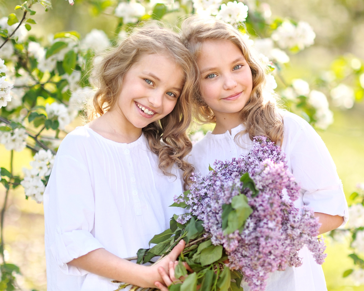 Две улыбающиеся девочки близняшки с букетом сирени