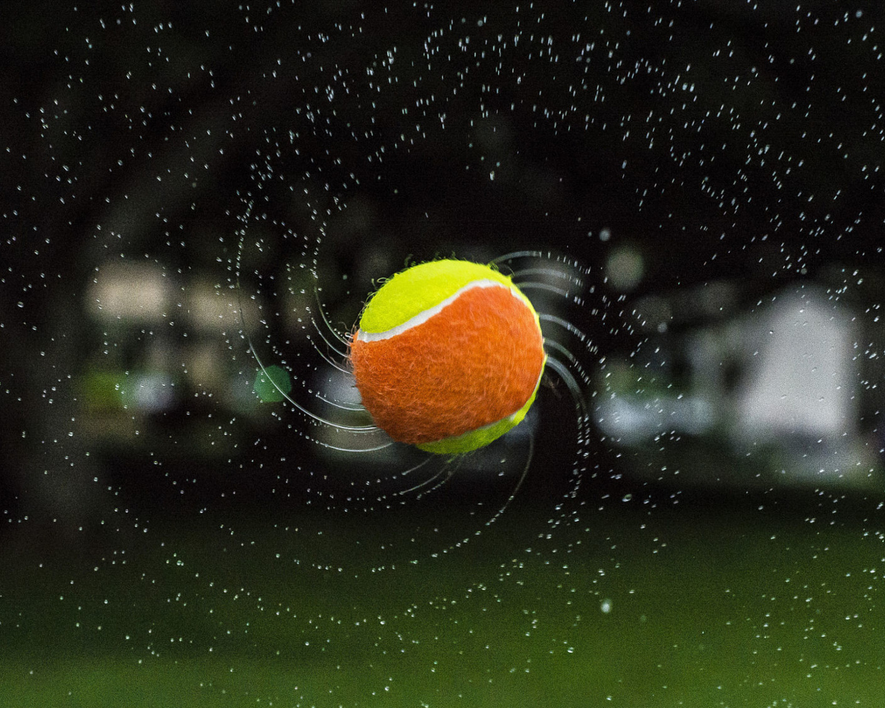 Теннисный мяч летит в каплях воды 