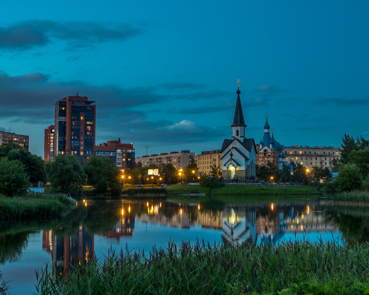 Вечерние огни маленькой церкви и домов отражаются в воде городского пруда, Санкт-Петербург. Россия