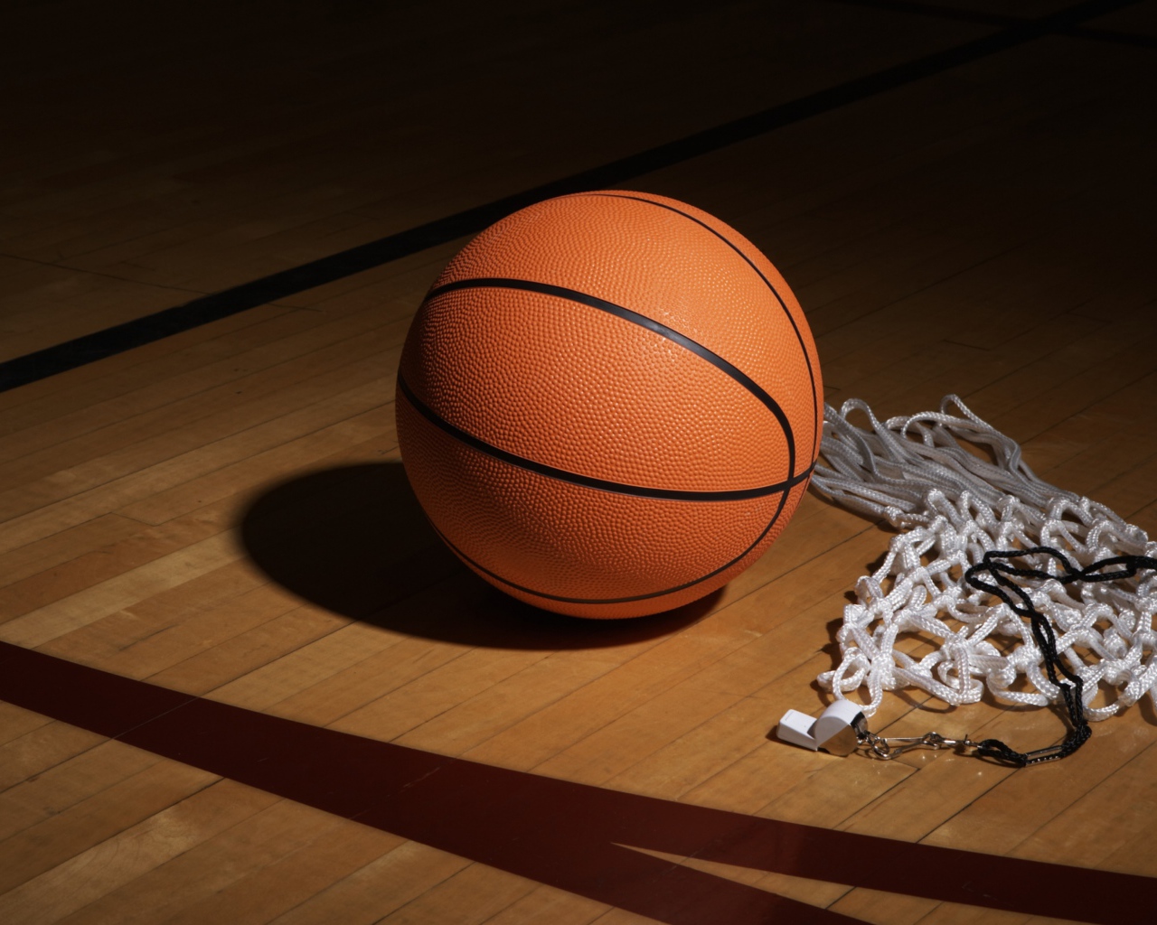 Баскетбольный мяч, свисток  и сетка на полу в спортзале 