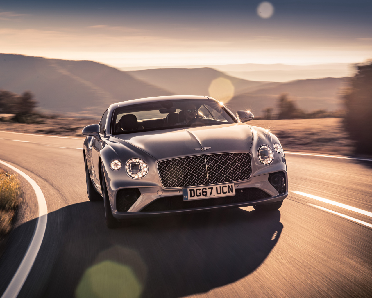 Серебристый автомобиль Bentley Continental GT 2018 года на трассе