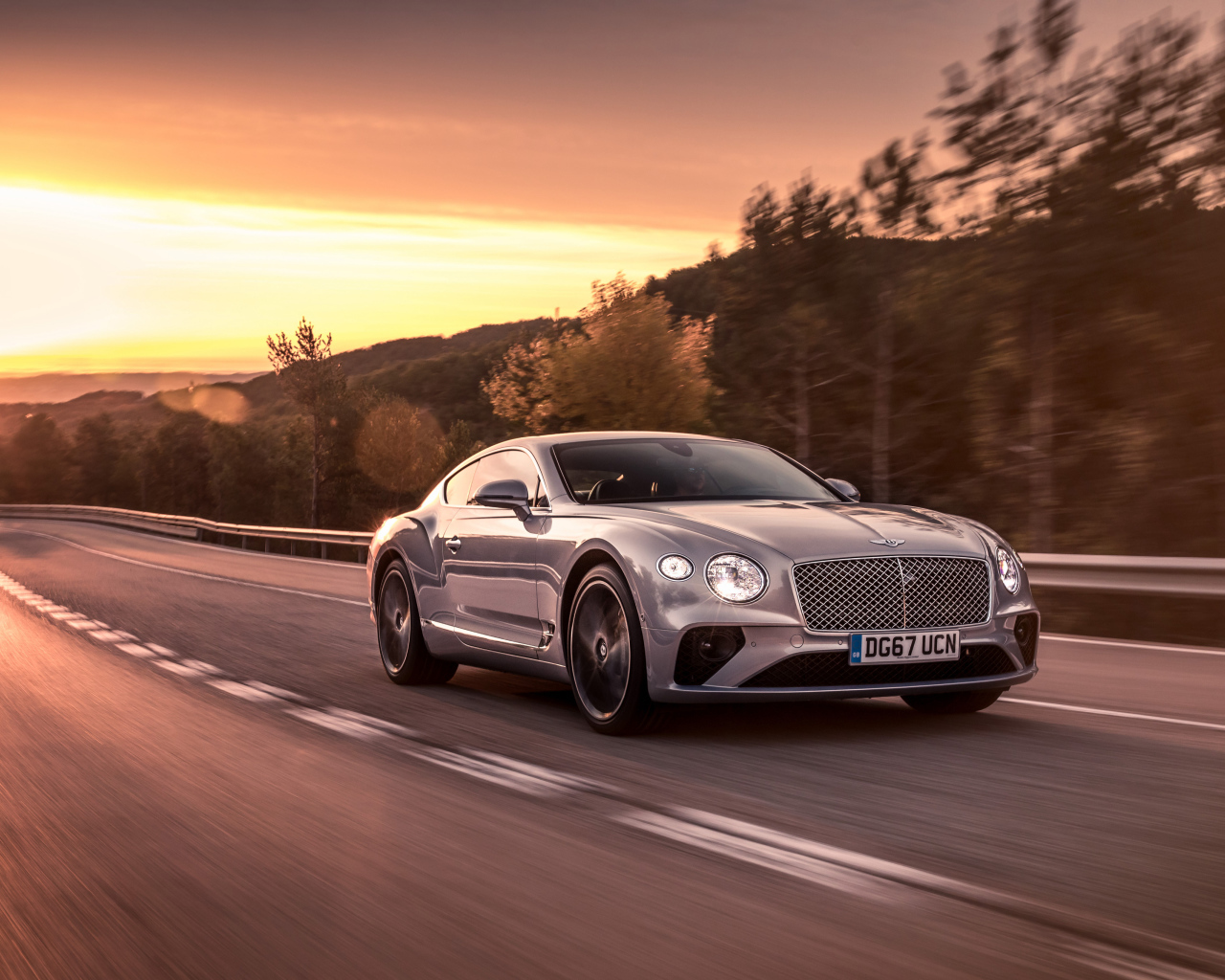 Серебристый автомобиль Bentley Continental GT 2018 года на фоне заката