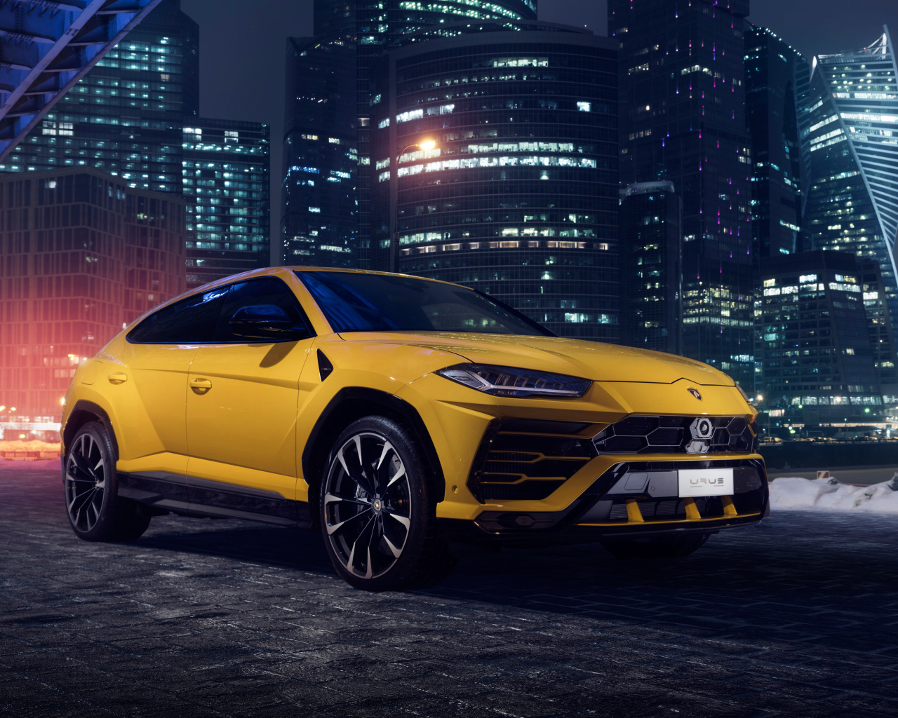Желтый Lamborghini Urus на фоне ночных небоскребов