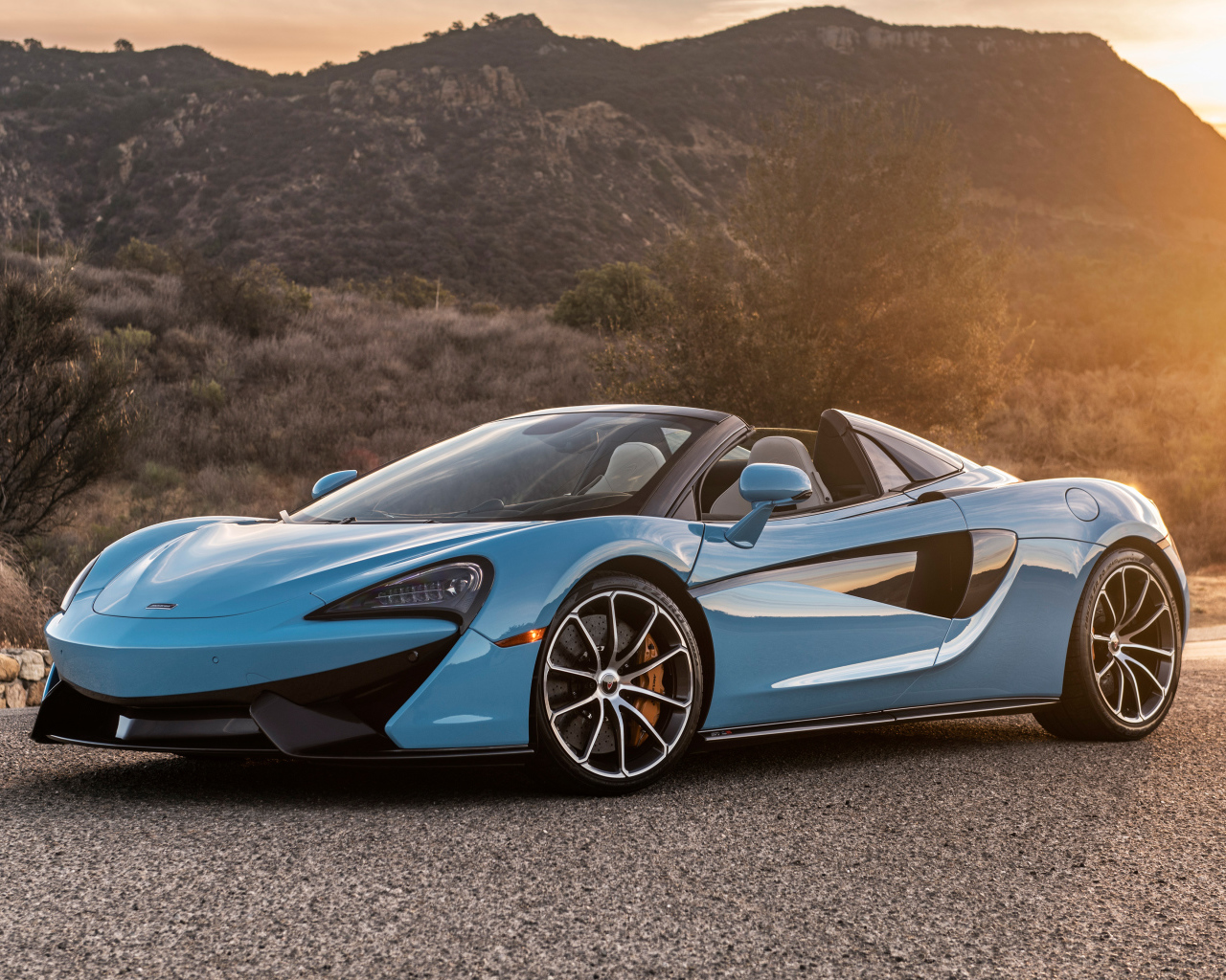 Голубой спортивный автомобиль  McLaren 570S Spider, 2018 на фоне солнца