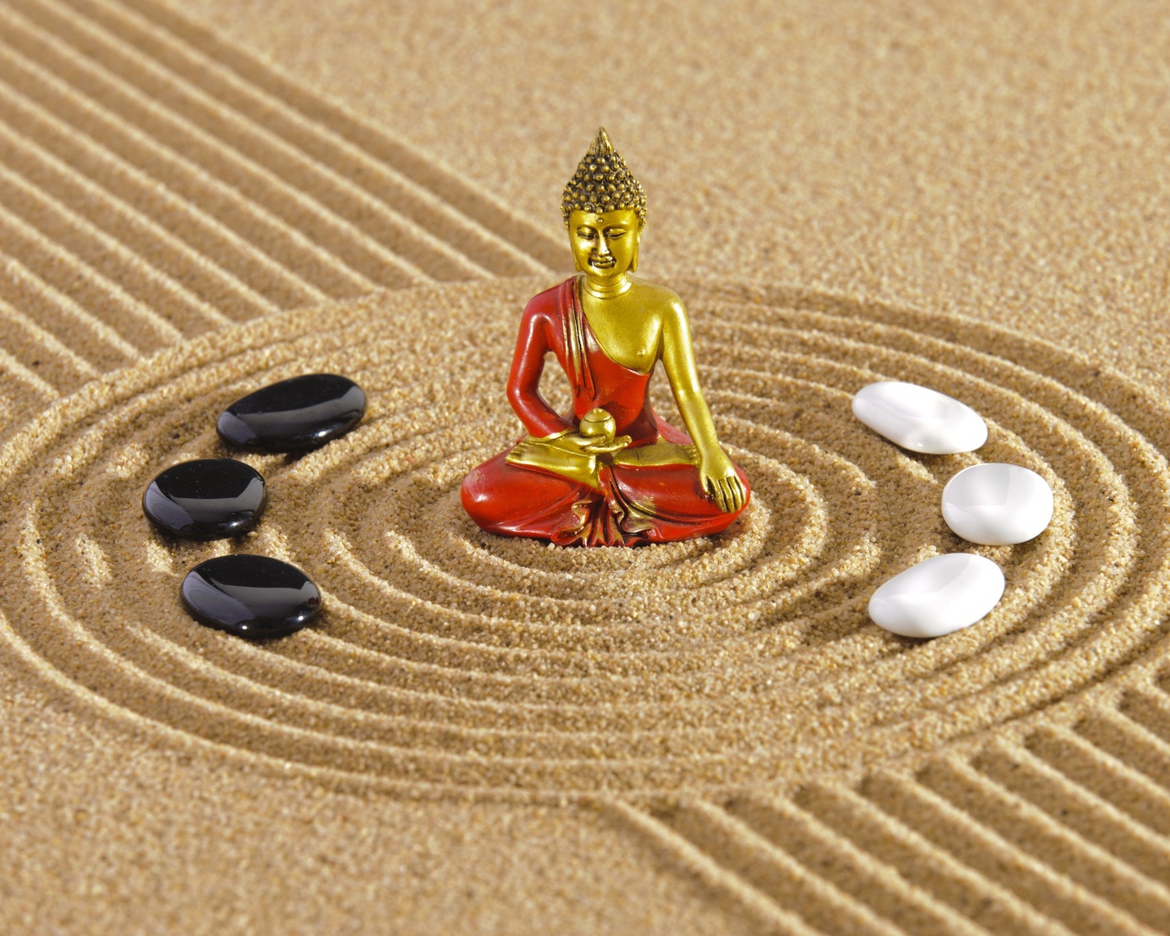 Статуэтка Будды стоит на песке с рисунком и камнями