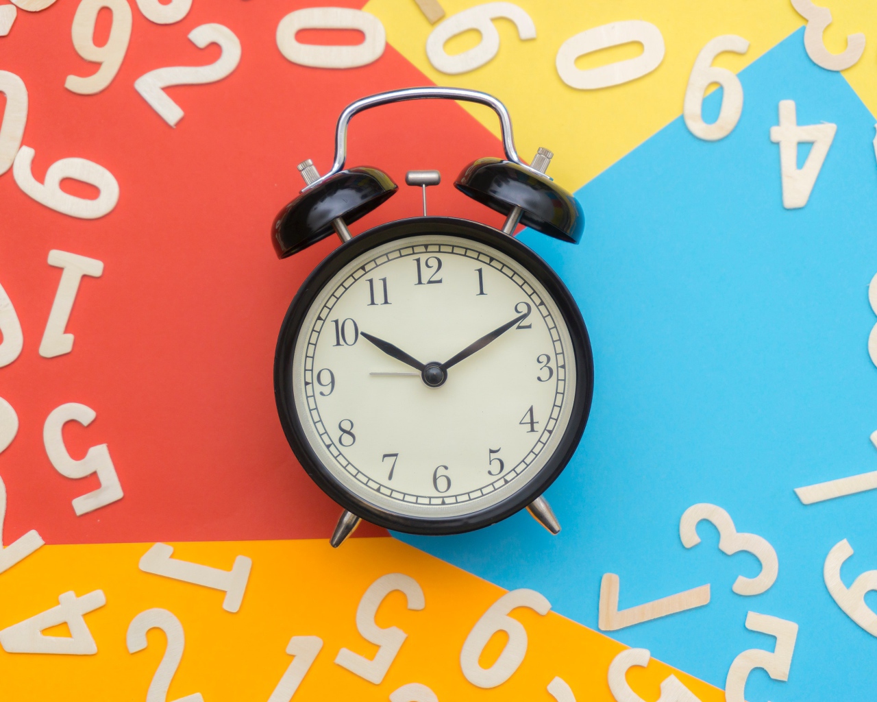 Будильник на разноцветном фоне с цифрами