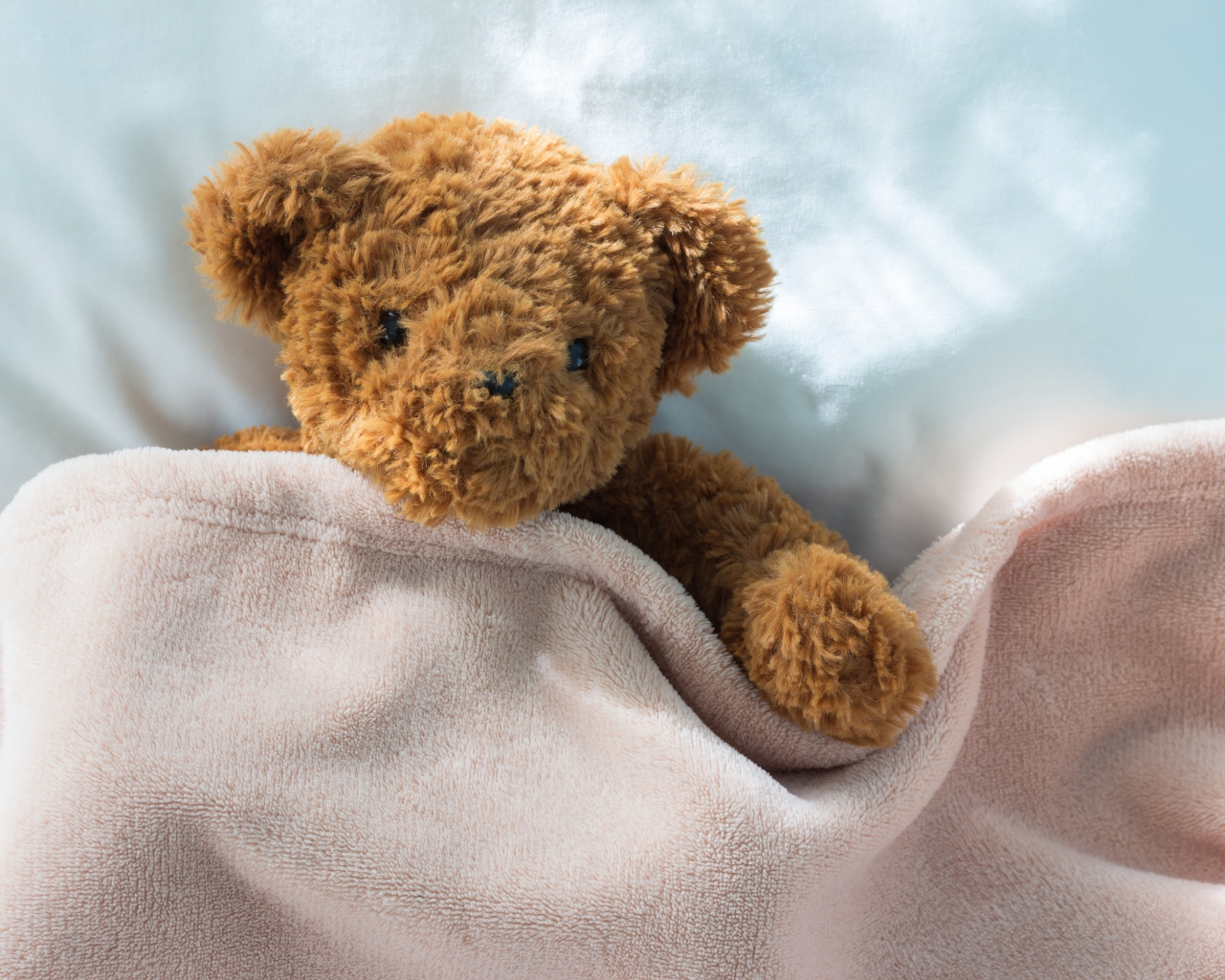 Плюшевый медведь в кровати под одеялом