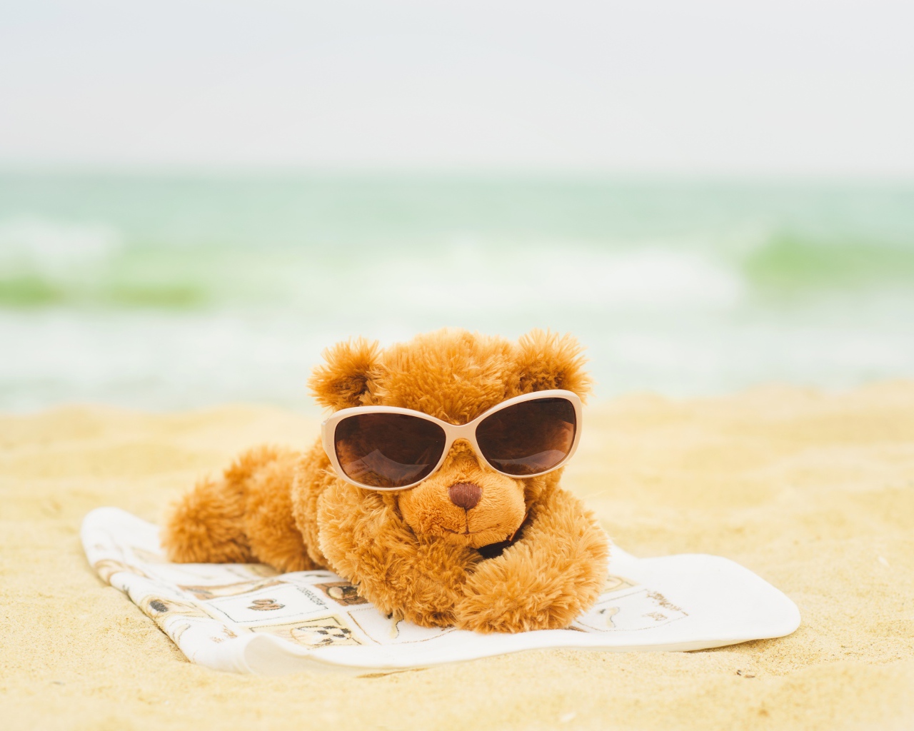 Плюшевый мишка в солнечных очках лежит на пляже