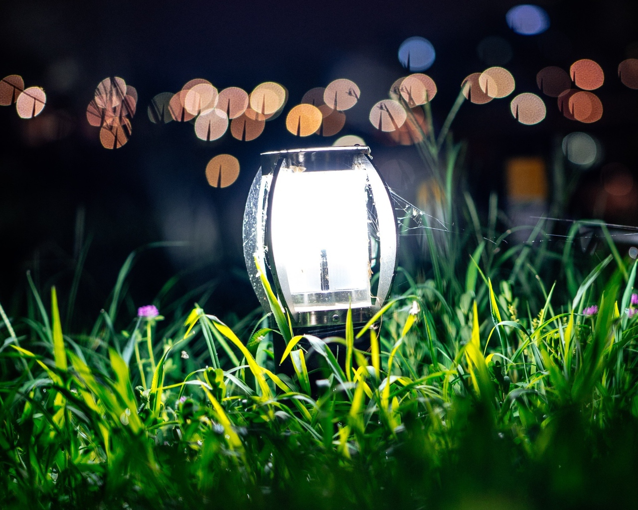 Включенный фонарь стоит в зеленой траве