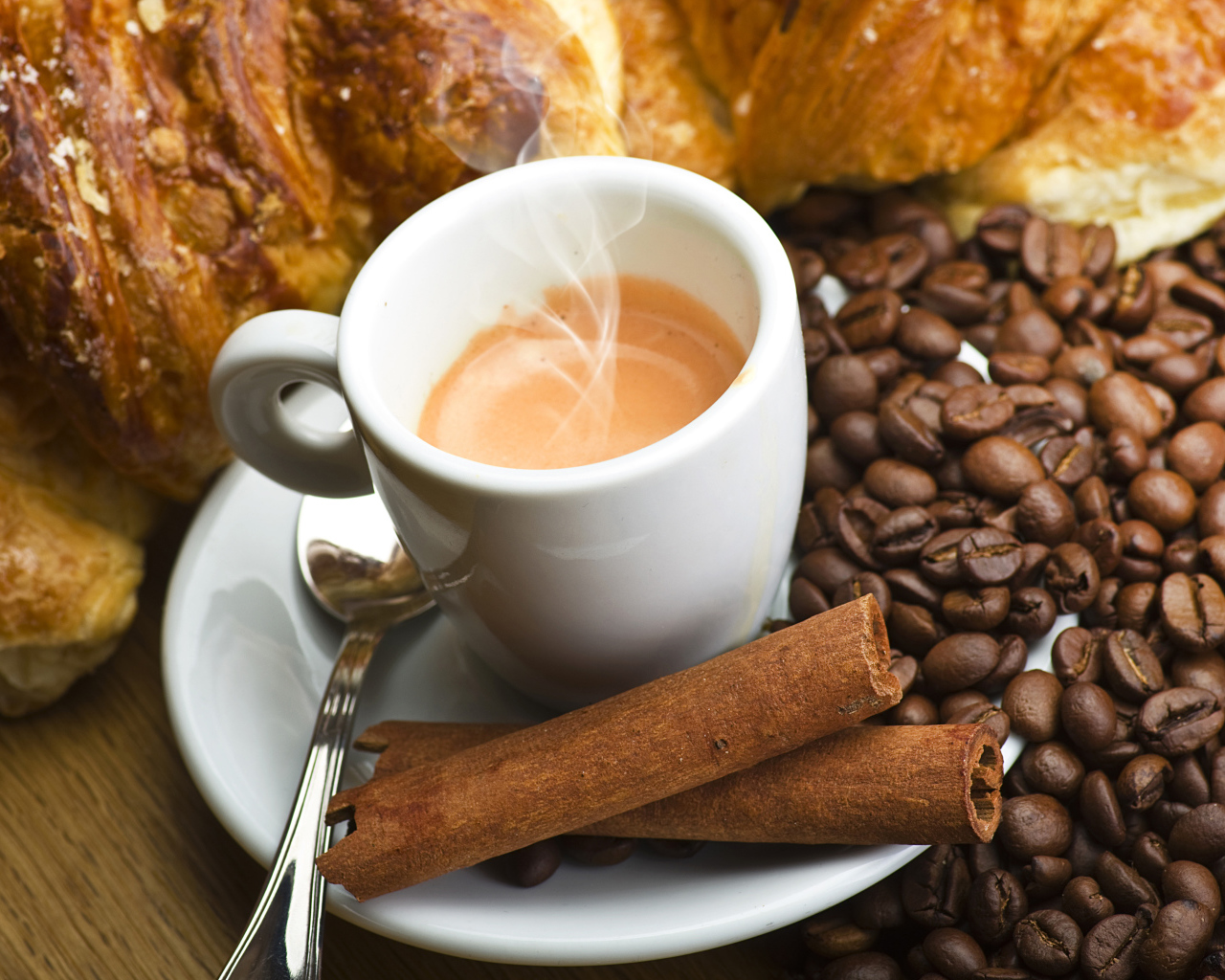 Чашка с горячим кофе на столе с корицей, зернами кофе и выпечкой