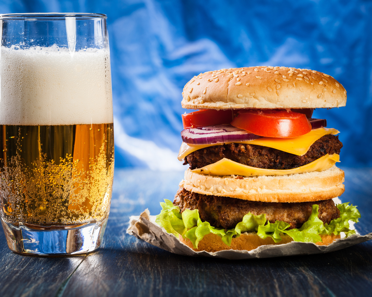 Стакан пива с гамбургером на столе