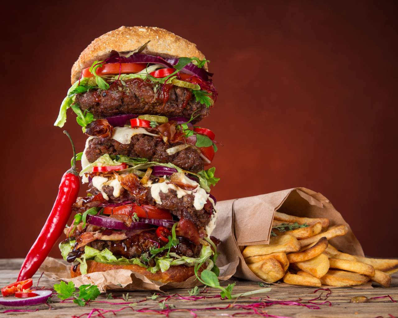 Огромный гамбургер на столе с картофелем фри и острым перцем