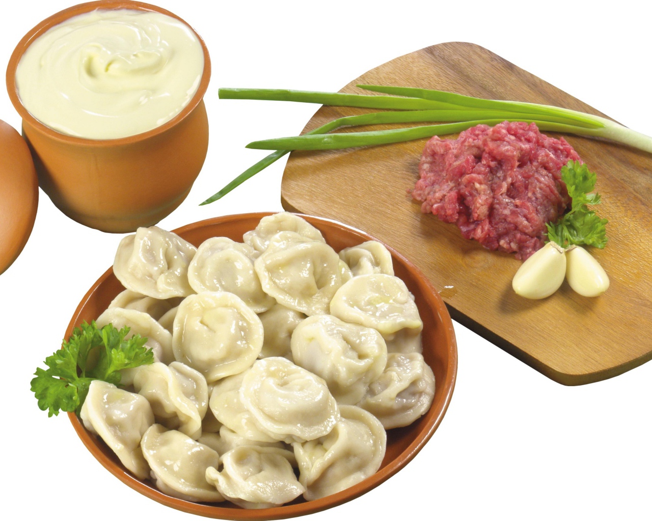 Вареные пельмени на столе с фаршем, сметаной и зеленым луком