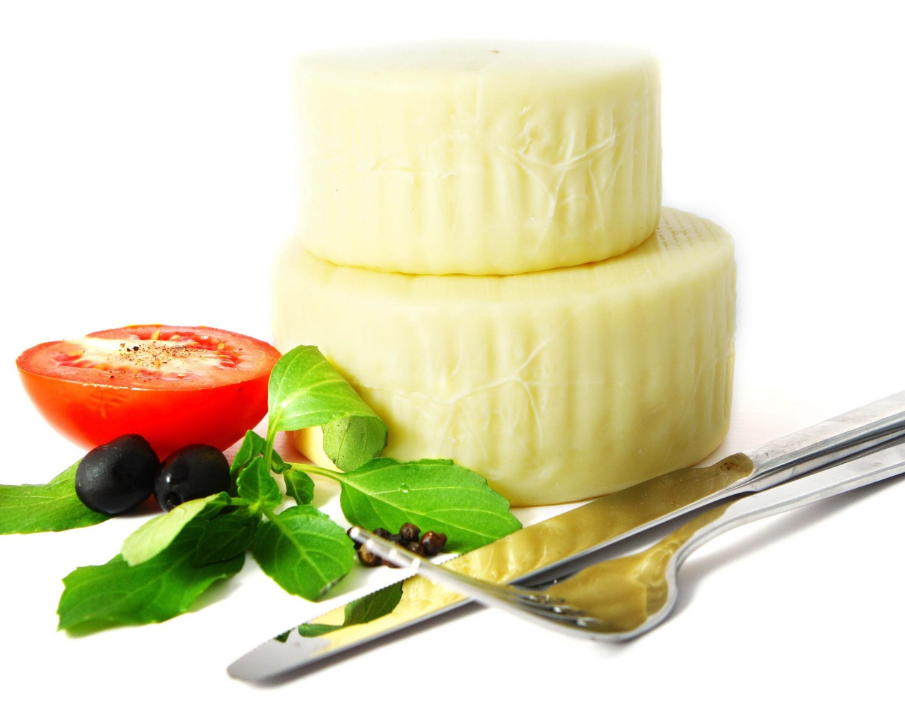 Сыр с помидором, столовыми приборами, оливками и зеленью на белом фоне