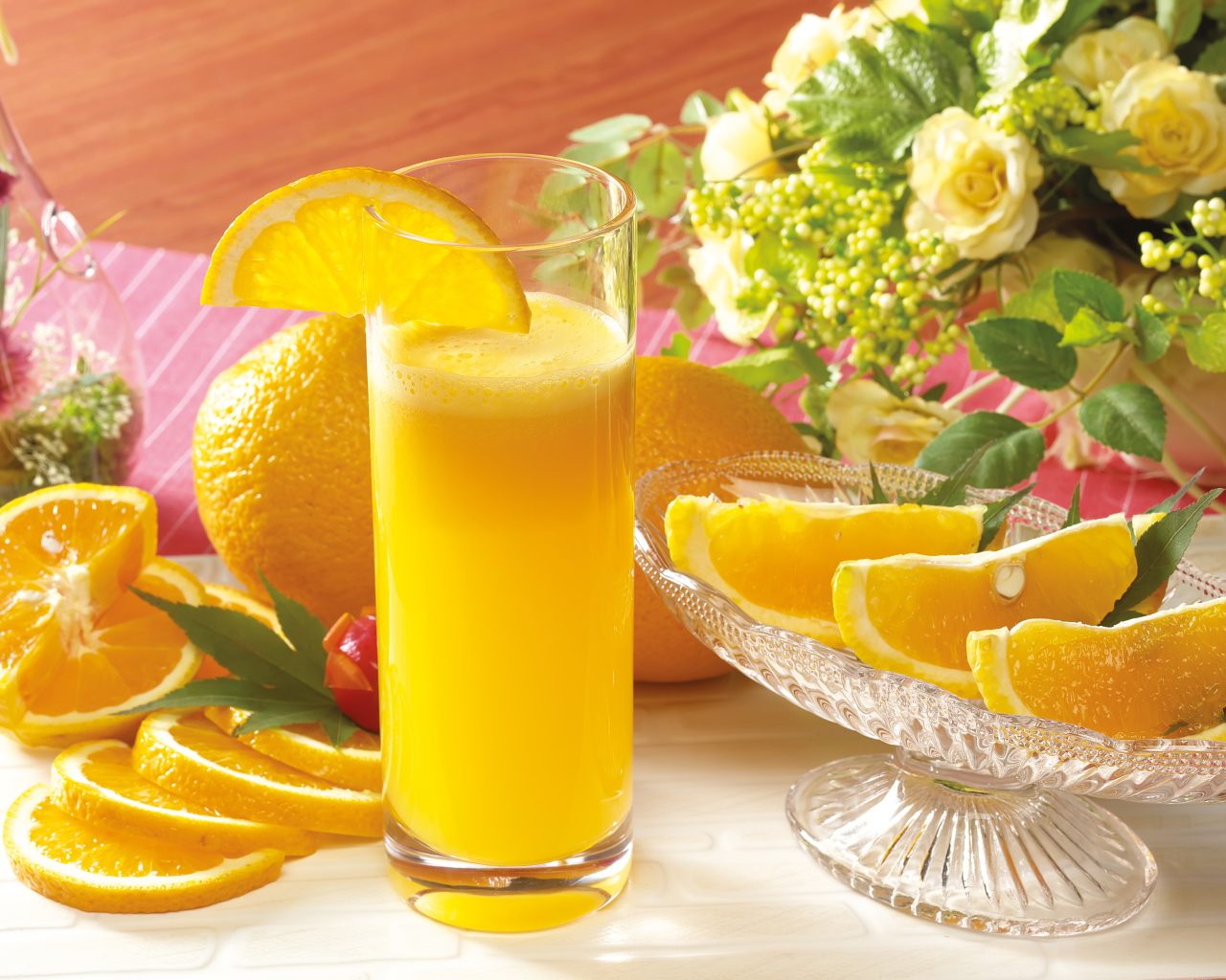 Свежий апельсиновый сок на столе с фруктами и цветами