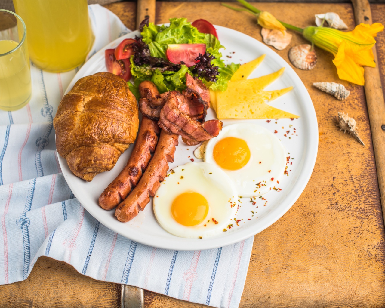 Яичница, салат, сосиски и круассан с соком на завтрак 