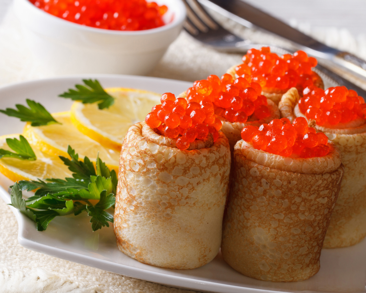 Блины с красной икрой на тарелке с лимонами и петрушкой