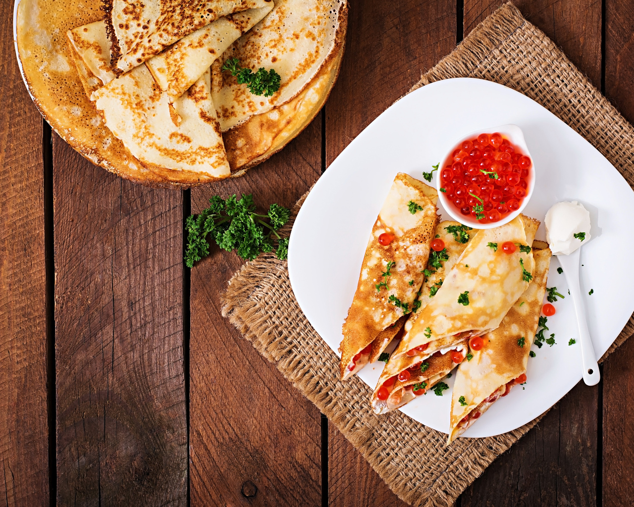 Рулетики из блинов на белой тарелке с красной икрой 