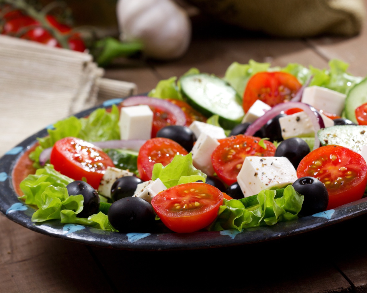 Салат с помидорами, огурцами, оливками, кусочками сыра и луком на листьях салата