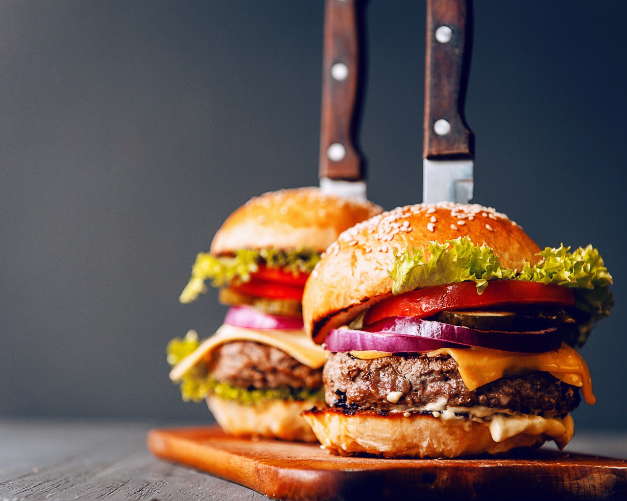 Два гамбургера с ножами на разделочной доске 