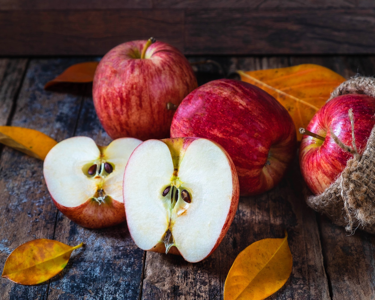 Красивые красные яблоки на столе с желтыми листьями