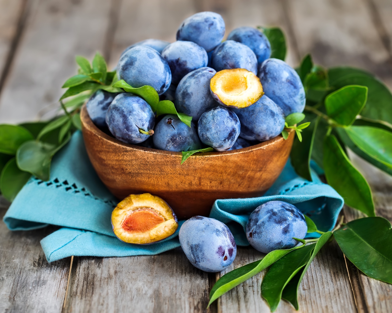 Синие сливы в деревянной миске с зеленой листвой
