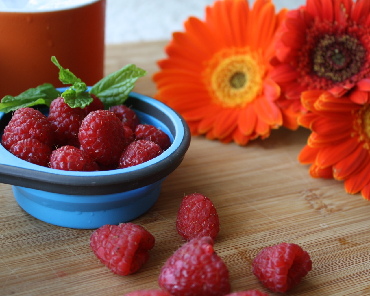 Свежая малина на столе с цветами герберы