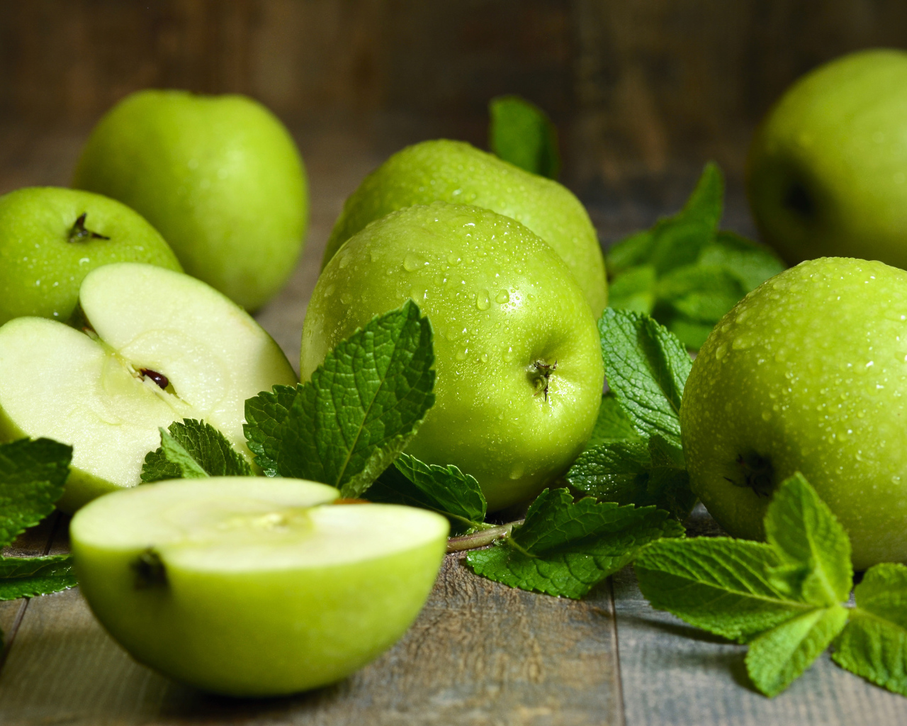 Зеленые яблоки в каплях воды на столе с мятой