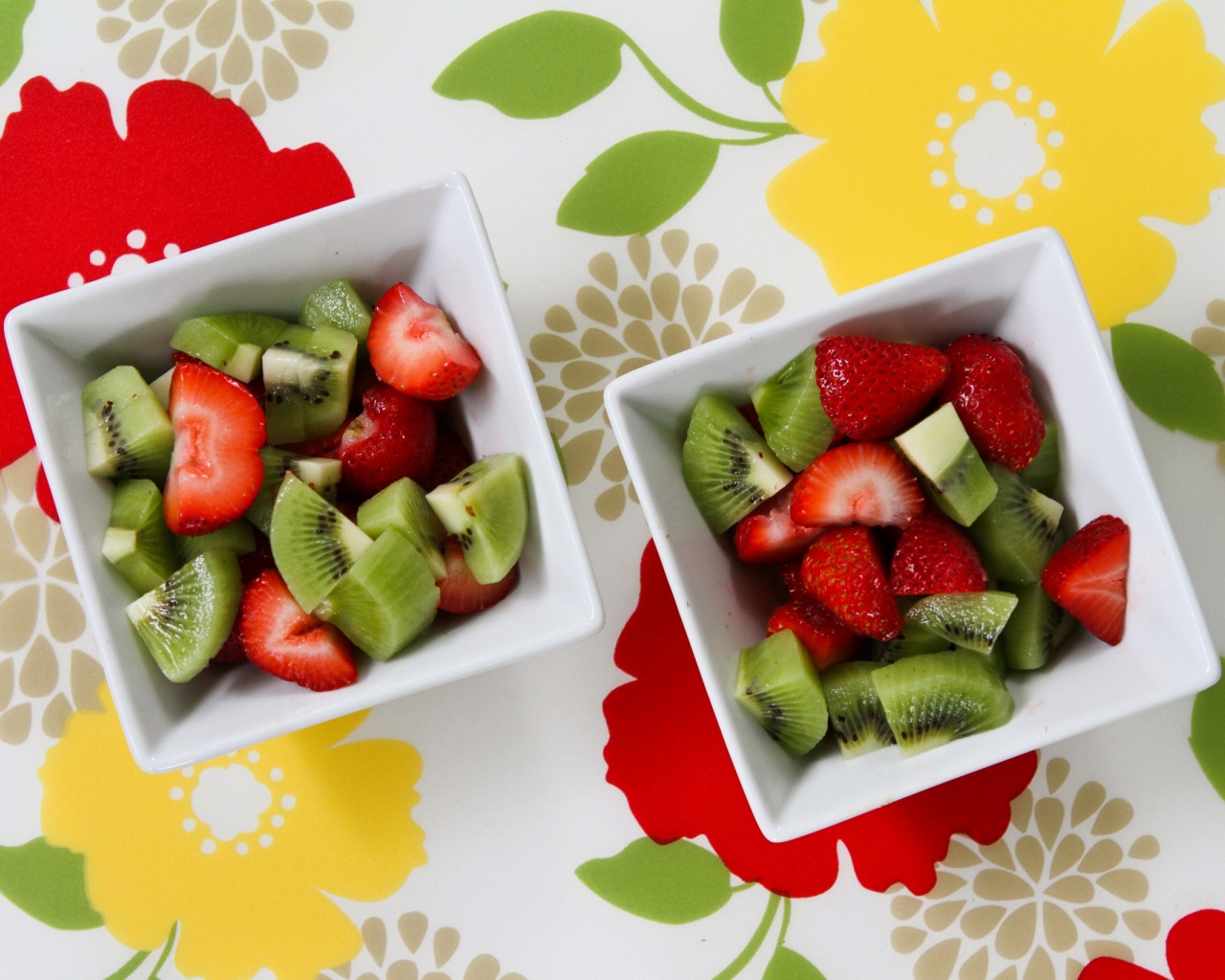 Салат с ягодами клубники и киви в белых тарелках на столе 