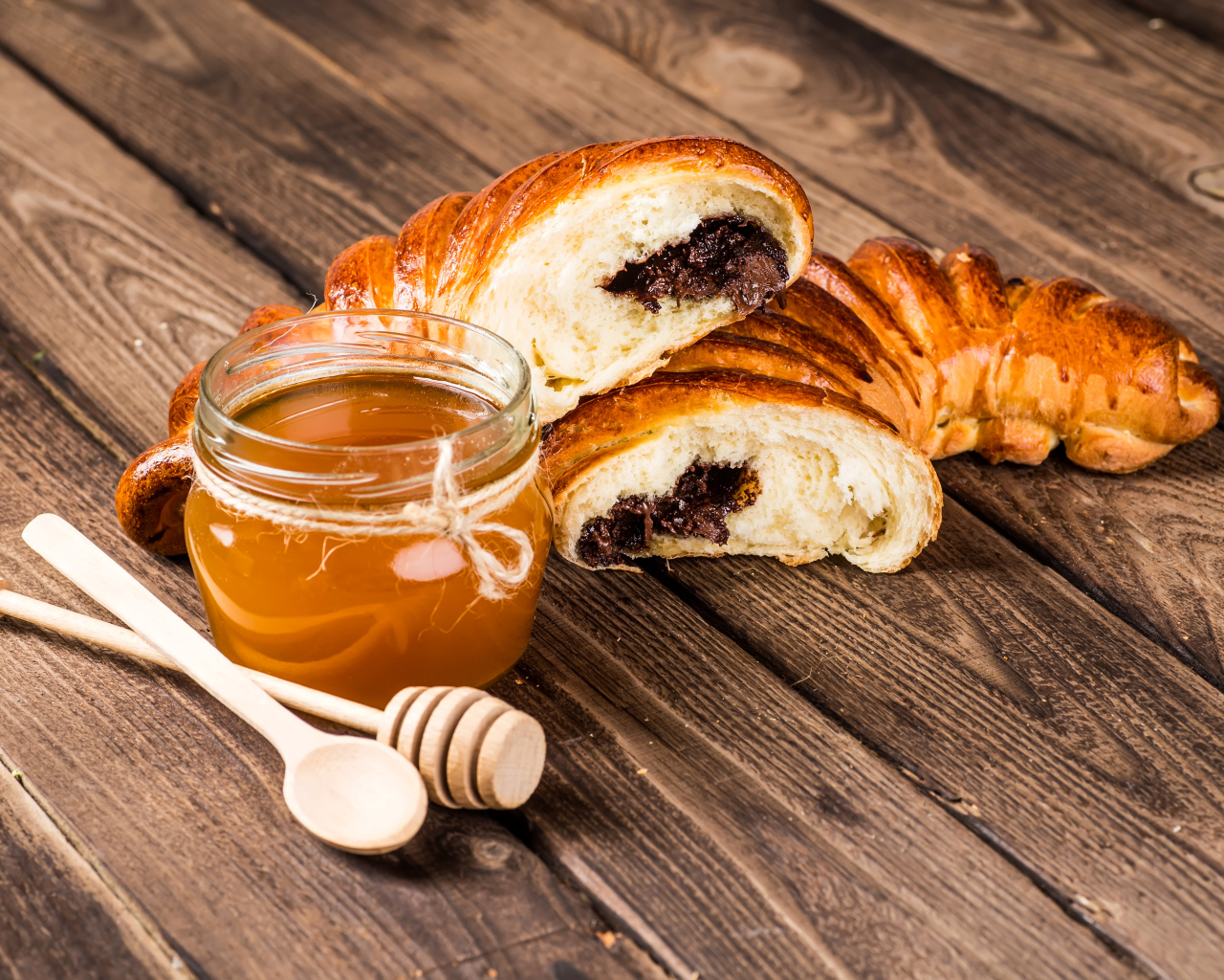 Банка меда, свежая выпечка и ложки на деревянном столе