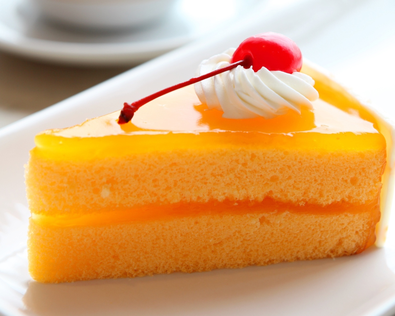 Кусок апельсинового торта с вишенкой на белой тарелке
